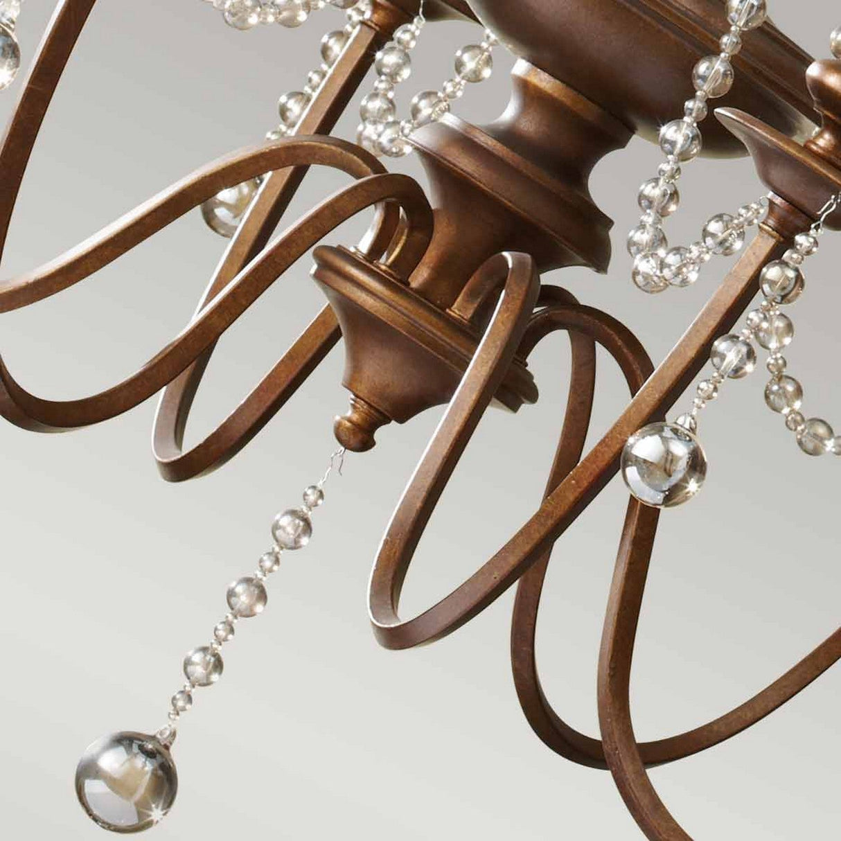 A close-up of the Feiss Clarissa 6 Light Chandelier - Firenze Gold highlights its swirling bronze metalwork and strings of champagne-plated glass beads, with the elegant design enhanced by its luxurious finish.