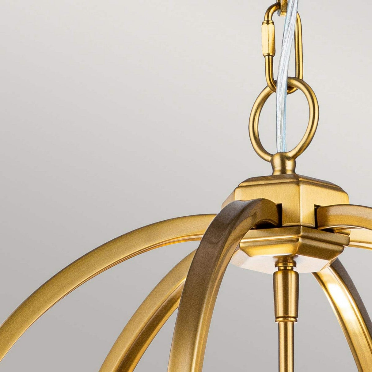 A close-up of the Corinne 3 Light Medium Chandelier in burnished brass reveals its elegantly curved metallic arms. It is suspended from a loop and wire against a neutral, light background, combining modern elegance with mid-century design elements.