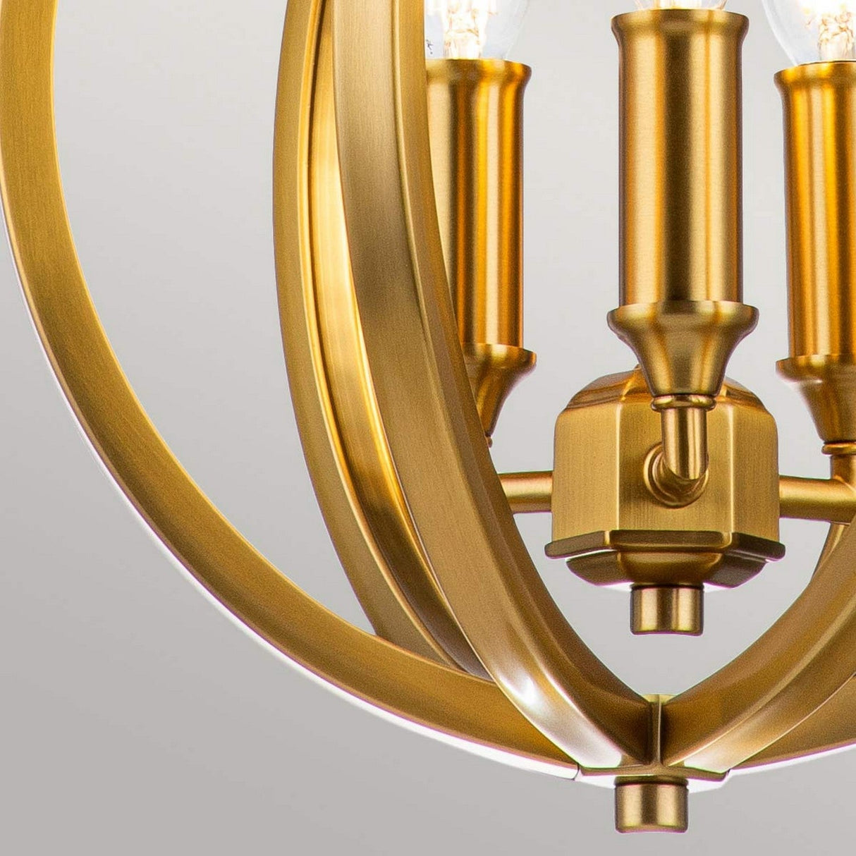 Close-up of the Corinne 3 Light Small Chandelier in burnished brass, showcasing its elegant circular design and visible light bulbs. The fixture features polished metal detailing and a sleek finish, set against a neutral background. This sophisticated chandelier enhances any space with its elegance.