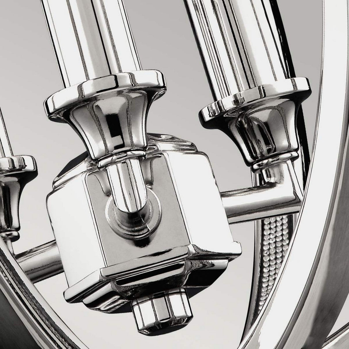 Close-up of the Corinne 3 Light Small Chandelier in polished nickel with its central hexagonal piece and cylindrical rods. The image showcases its polished surfaces reminiscent of a modern lighting fixture, highlighting intricate engineering details in a sleek design.