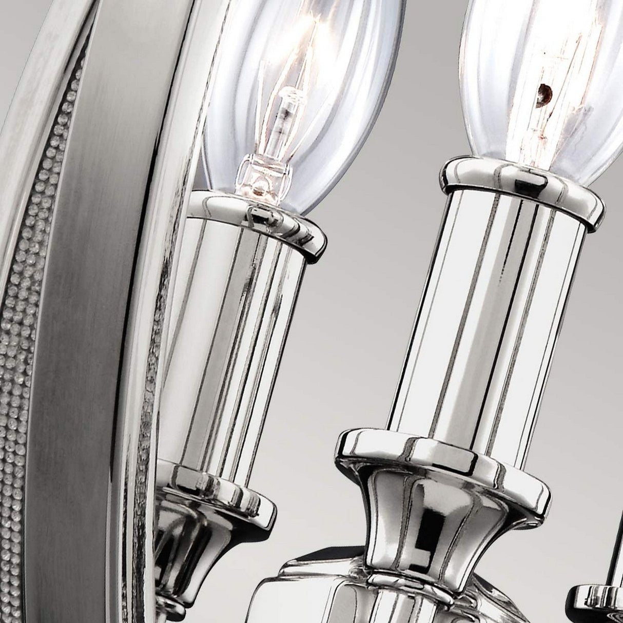 Close-up of the Corinne 3 Light Small Chandelier in polished nickel, featuring two small, clear glass incandescent bulbs. The sleek finish beautifully captures soft reflections of light.