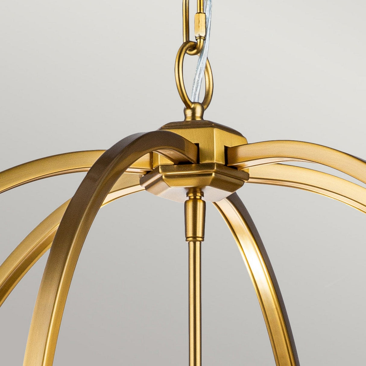 A close-up of the Corinne 6 Light Chandelier in burnished brass showcases its modern design, featuring elegant, curved arms. This fixture has several metallic arches extending from a central hub, forming an open orb silhouette. The warm golden hue stands out beautifully against the neutral light background.
