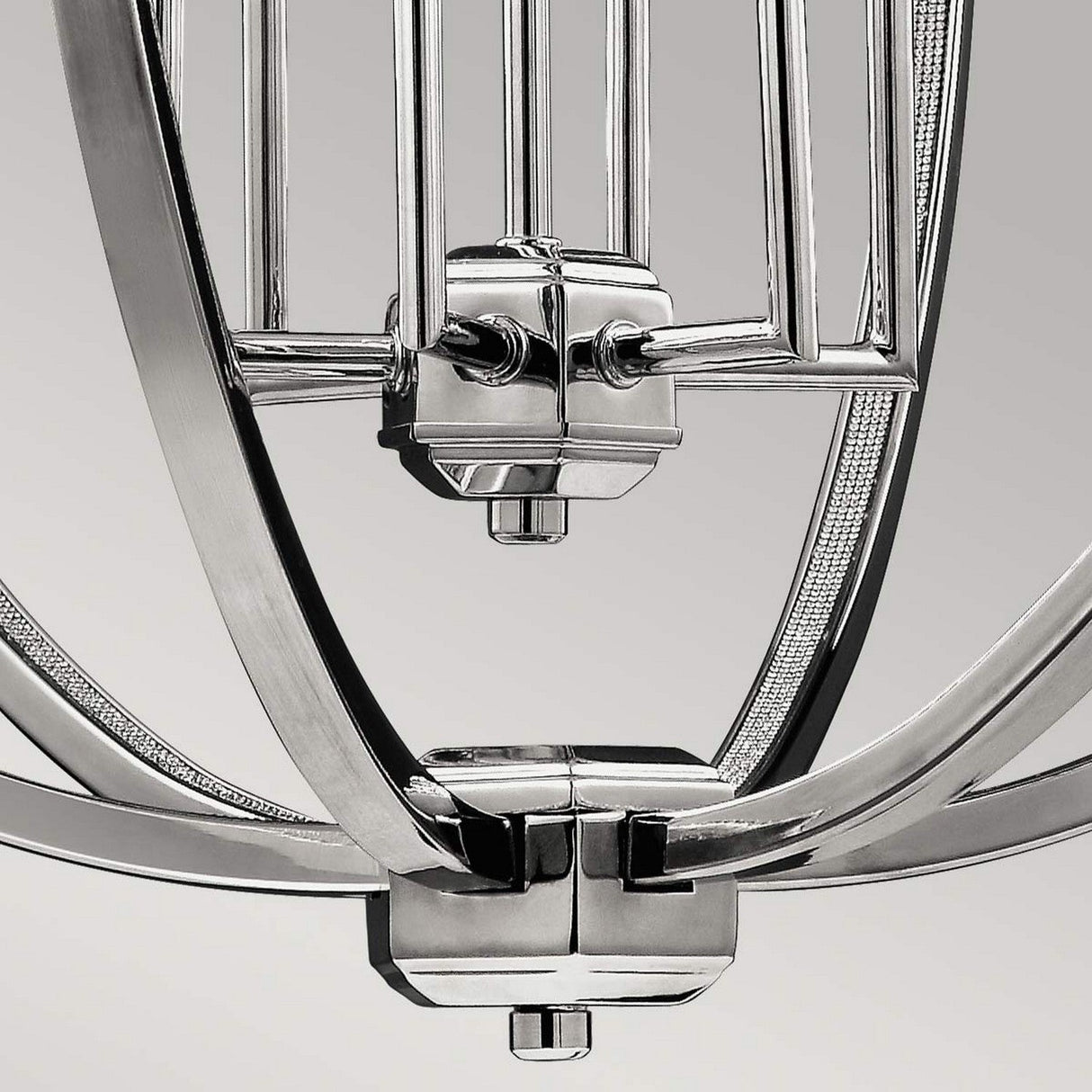 A close-up reveals the Corinne 6 Light Chandelier in polished nickel, showcasing a modern industrial elegance with its sleek metallic geometric design against a plain gray background.