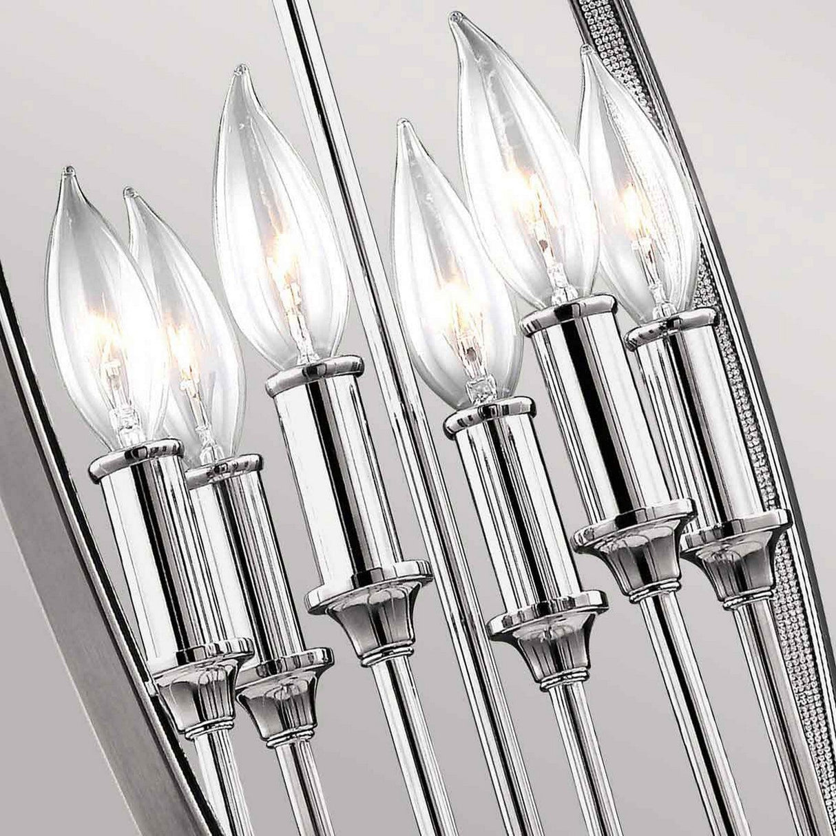 A close-up of the Corinne 6 Light Chandelier in polished nickel features six lit candle-shaped bulbs, exuding modern elegance. The chandelier’s polished nickel finish and clear glass bulbs beautifully reflect light, contributing to its bright and sophisticated appearance.