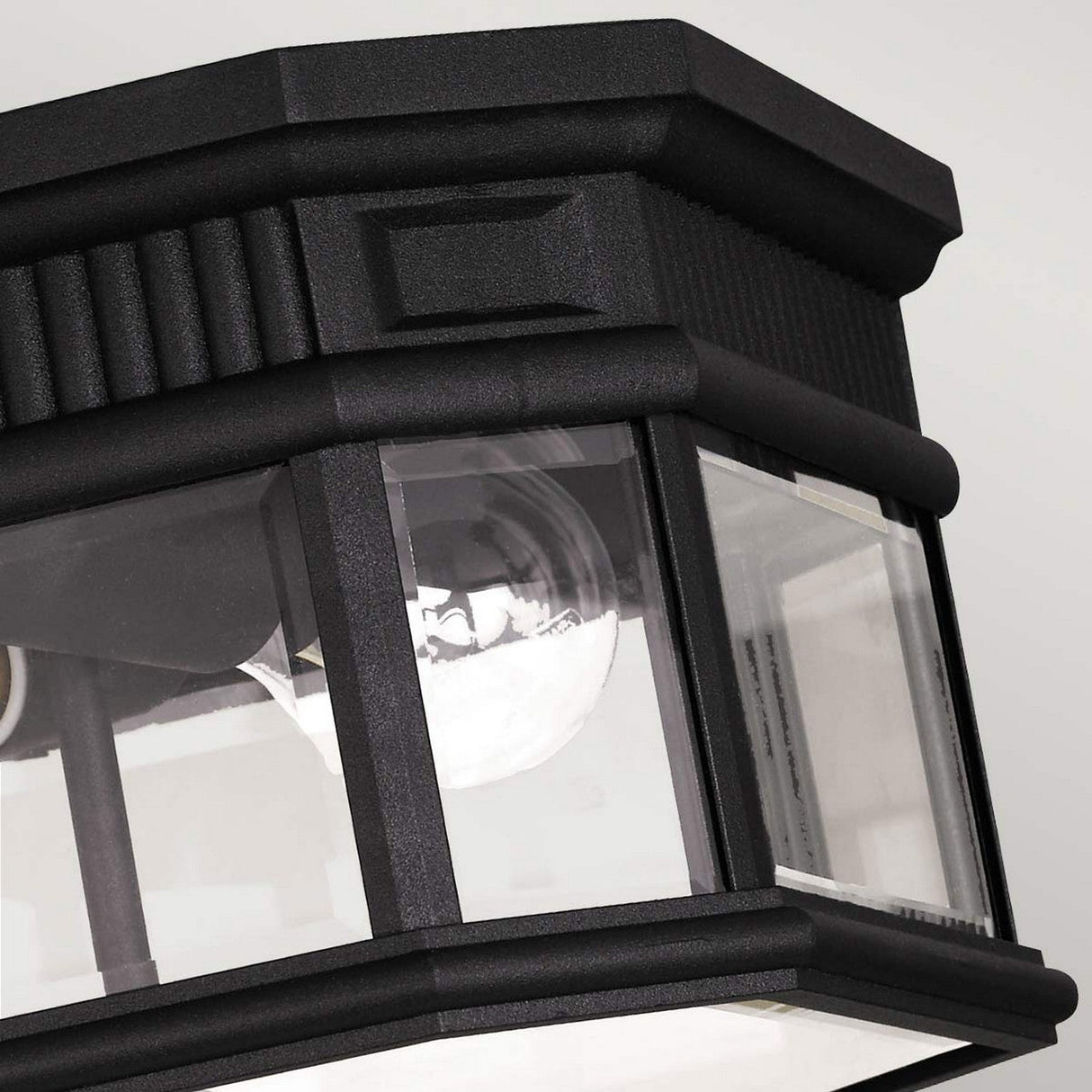 Close-up of the Cotswold Lane 2 Light Outdoor Flush in black, showcasing a ribbed design. It features transparent glass panels that reveal a single light bulb inside, set against a plain gray background.