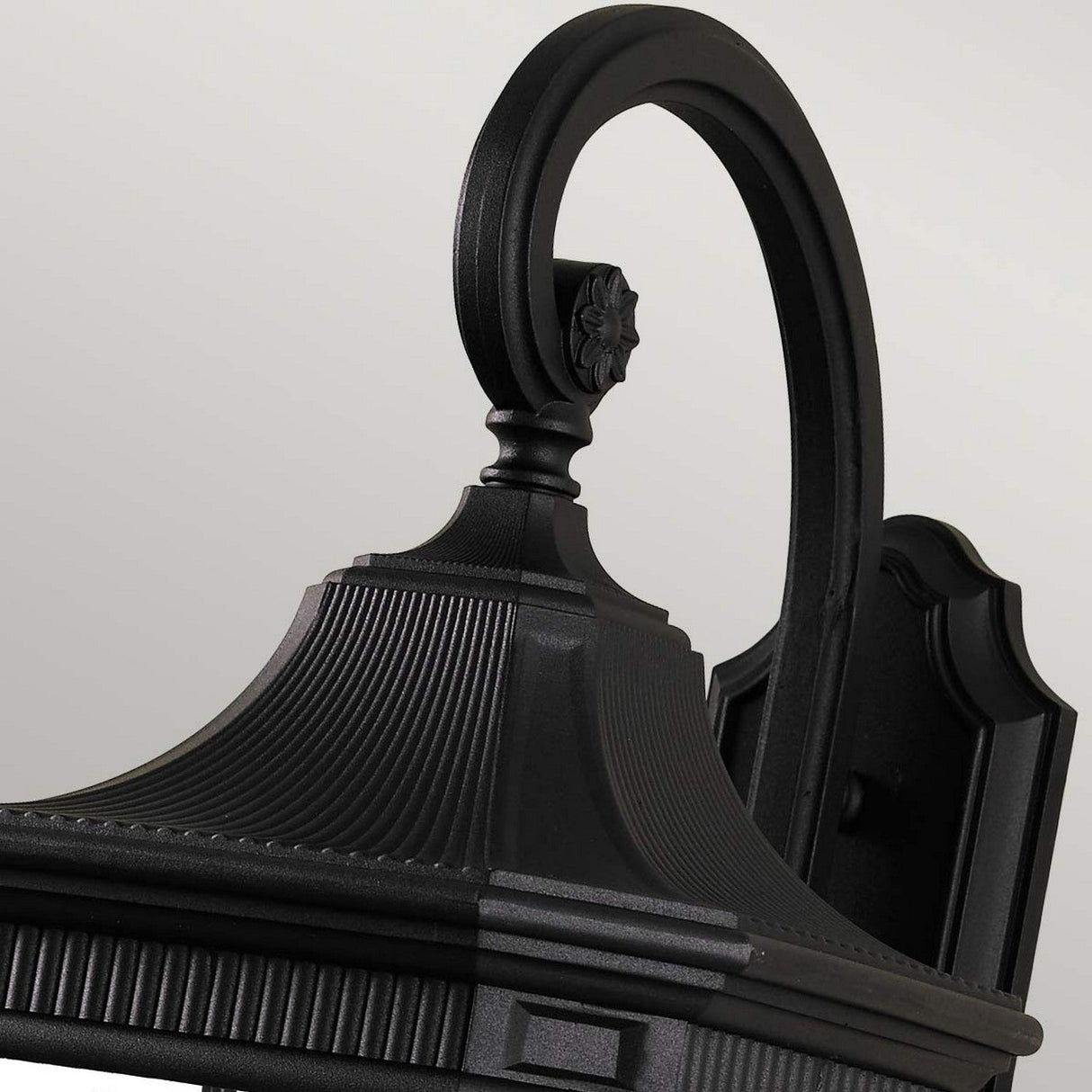 Close-up of a Cotswold Lane 3 Light Outdoor Large Wall Lantern in a black finish, showcasing its curved arm and decorative details against a neutral background. The lantern features a traditional design with ribbed texture and a floral accent on the top.