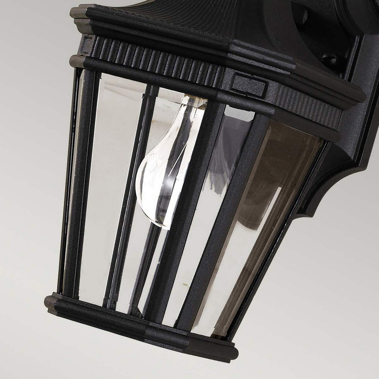 Close-up of the Cotswold Lane 1 Light Outdoor Small Wall Lantern in black, featuring a clear glass pane encasing a single visible bulb. The design highlights vertical metal bars and captures a classic, traditional aesthetic.