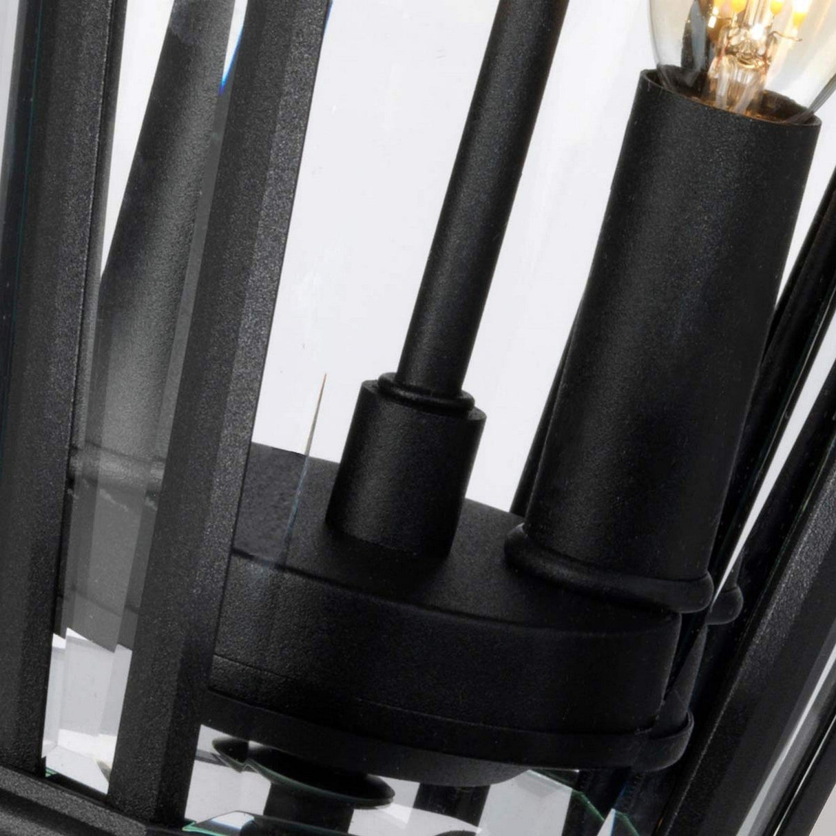 Close-up view of the black Cotswold Lane 2 Light Outdoor Medium Light fixture with bevelled glass panes. Inside, a visible light bulb glows softly, highlighting the fixture's industrial design and modern aesthetic reminiscent of antique gas lanterns.