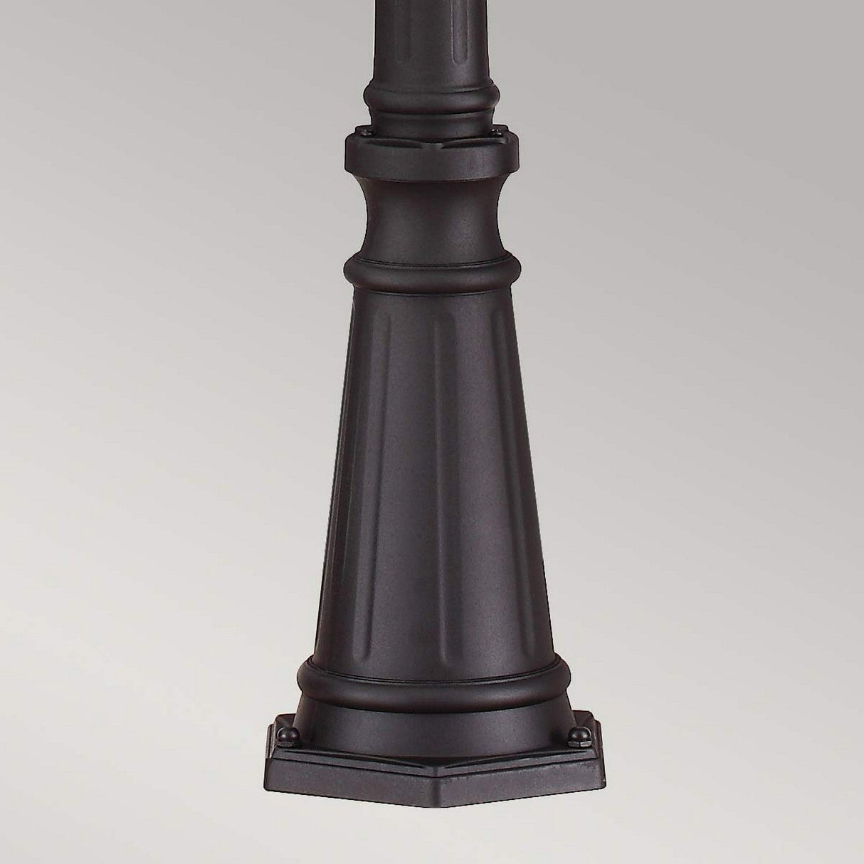 A detailed view of a black cylindrical pedestal with vertical grooves and a hexagonal base, reminiscent of the elegance captured by the Cotswold Lane 3 Light Large Post - Black, set against a plain gray background.
