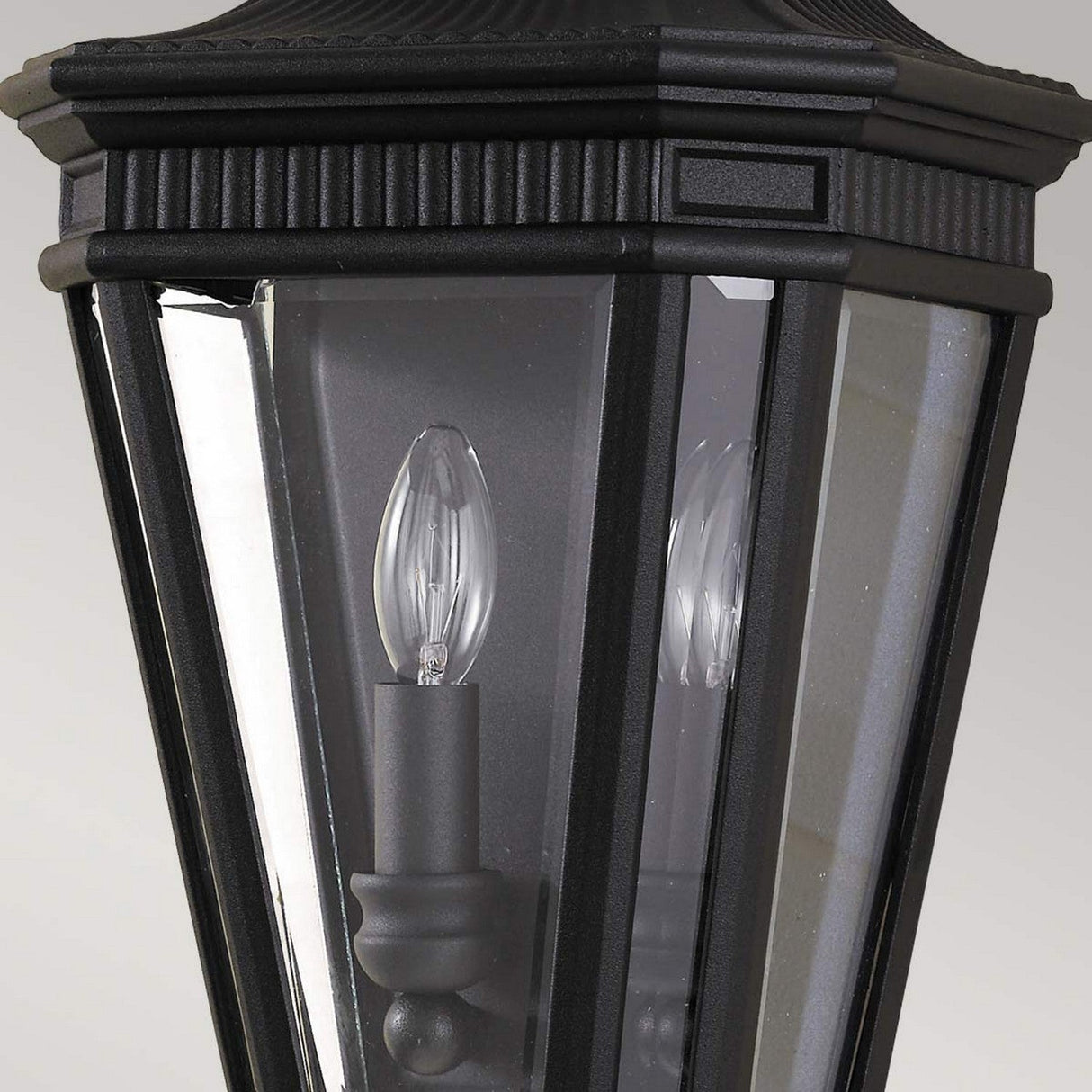 The Cotswold Lane 2 Light Outdoor Wall Lantern in black displays a classic design with a black finish and clear beveled glass. It features a candle-shaped bulb inside and decorative detailing at the top.