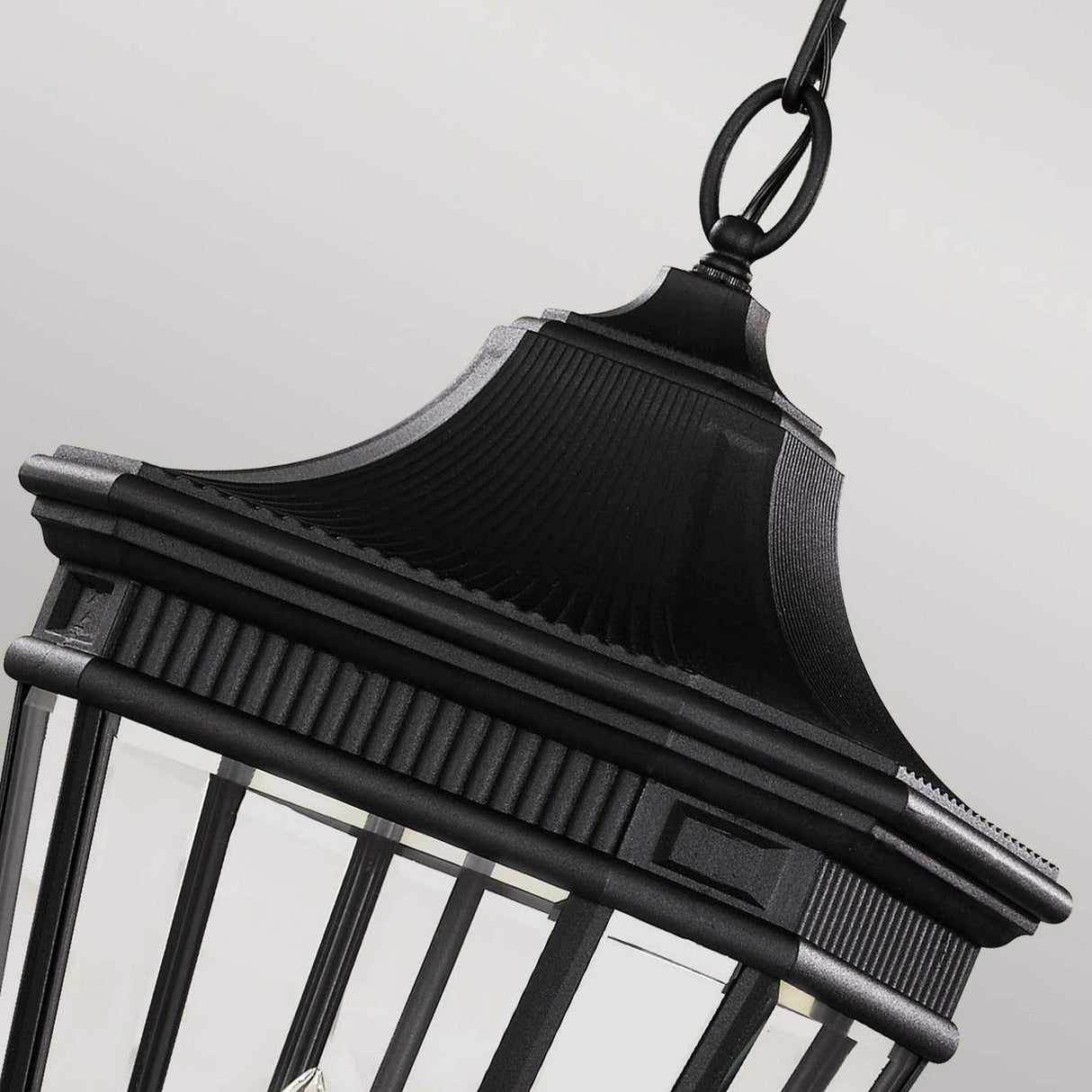 A close-up of the Cotswold Lane 3 Light Outdoor Large Chain Pendant in black showcases its vintage charm with a classic design. The pendant, complete with a chain for hanging and a glass enclosure around the light bulbs, stands out against a plain light gray background that enhances the elegance of this timeless outdoor lighting piece.