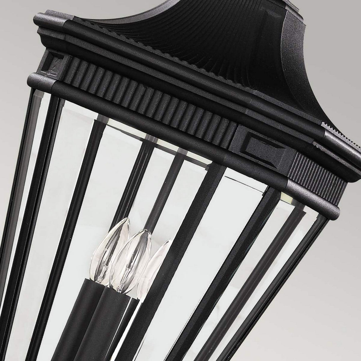 A close-up of the Cotswold Lane 3 Light Outdoor Large Chain Pendant in black reveals its vintage-style charm, featuring three candle-like bulbs inside clear glass panels. This lantern is perfect for outdoor lighting, standing out against a light gray background.