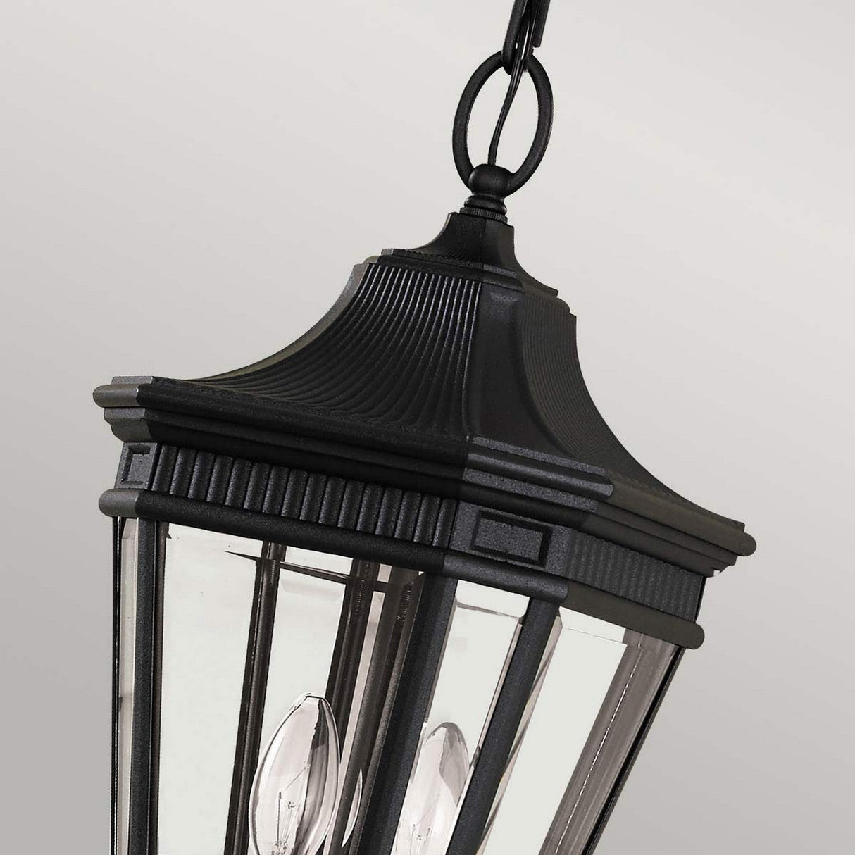 Close-up of the Cotswold Lane 2 Light Outdoor Medium Chain Pendant in black, showcasing its elegant design with a pointed top and clear glass panels that reveal its two-light setup. The black chain suspends the lantern gracefully against a plain gray background.