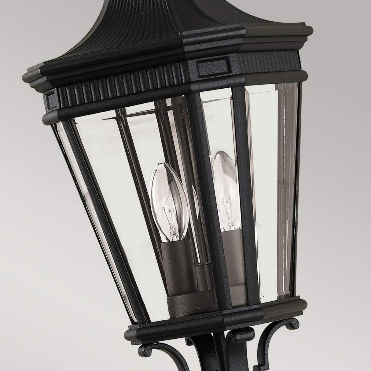 Close-up of the Cotswold Lane 2 Light Outdoor Medium Chain Pendant in black, featuring vintage styling with clear glass panels and a black chain. The pendant houses candle-shaped bulbs for a classic touch against a neutral gray background.