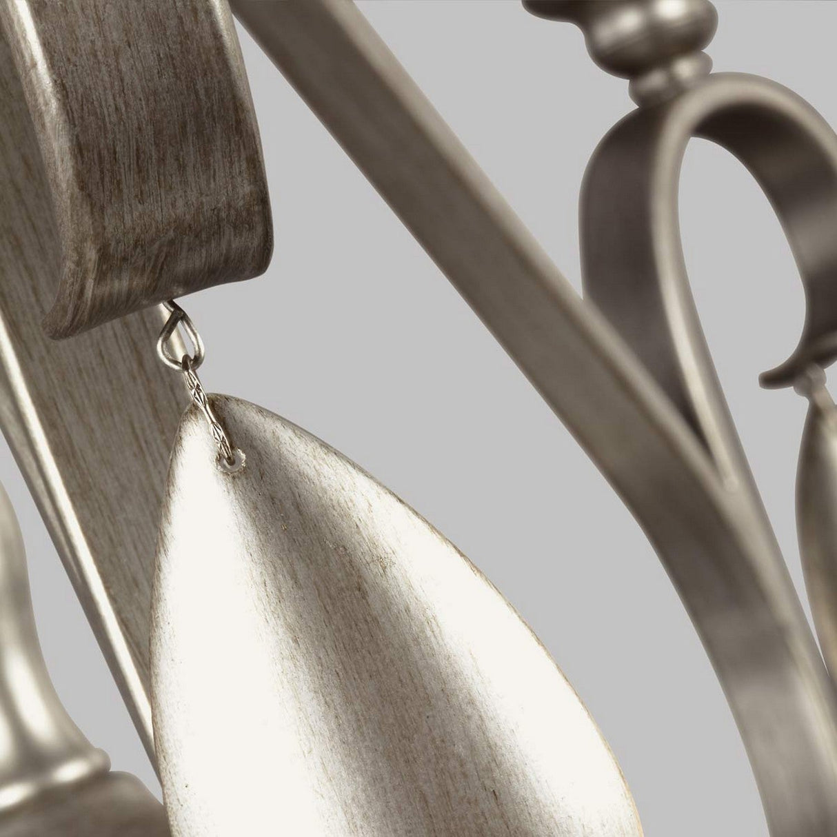 A close-up of the DeWitt 5 Light Chandelier reveals metallic fan blades with a wooden texture, elegantly suspended from an ornate, curved metal fixture that evokes French Provincial design. The neutral gray background highlights its chandelier-like elements, perfectly marrying sophistication with rustic charm.