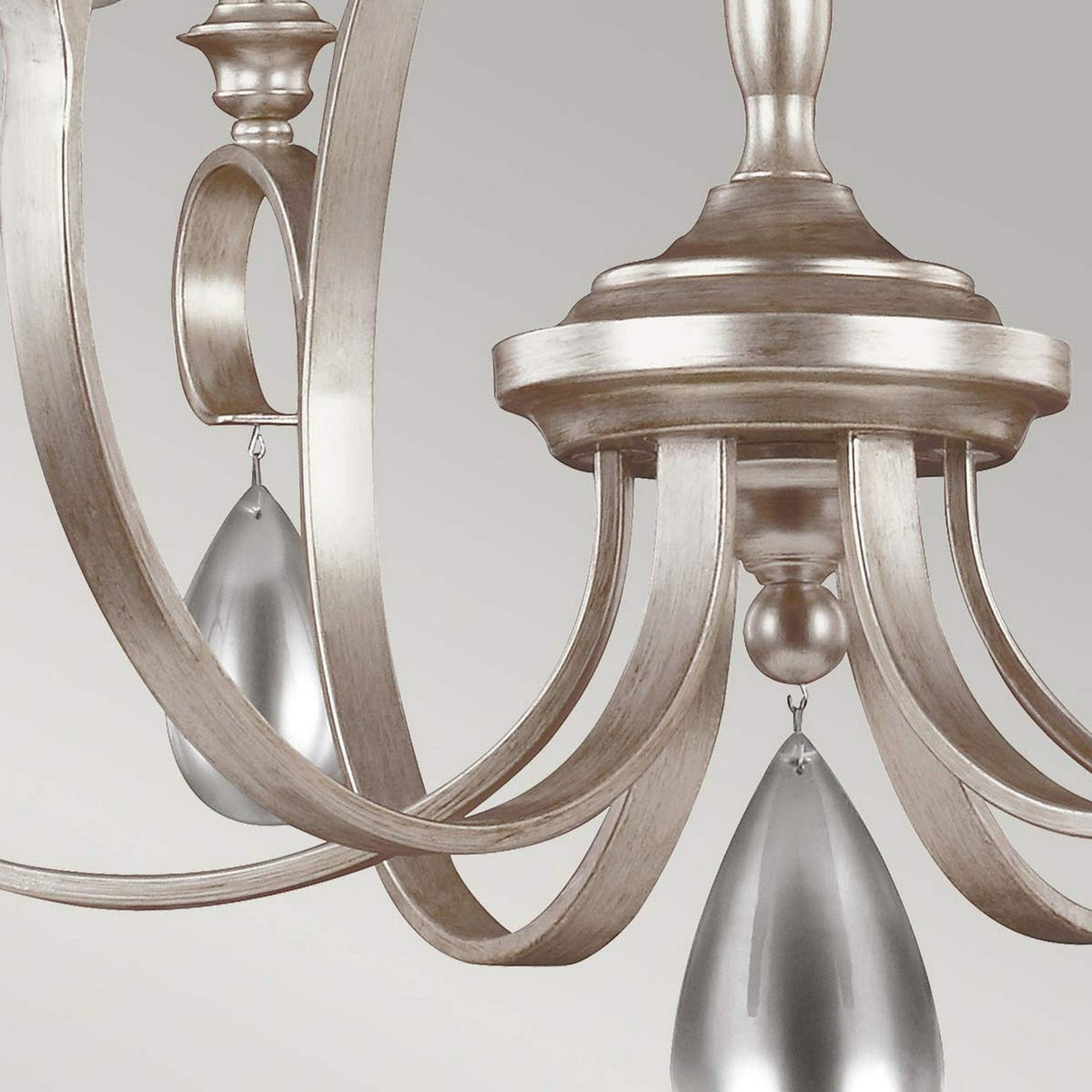 Close-up of the DeWitt 9 Light Chandelier - Silver, highlighting its ornate metallic design featuring elegant, curved arms and teardrop crystals. The chandelier's silvery finish perfectly complements its French Provincial aesthetic, elegantly suspended against a muted gray background.