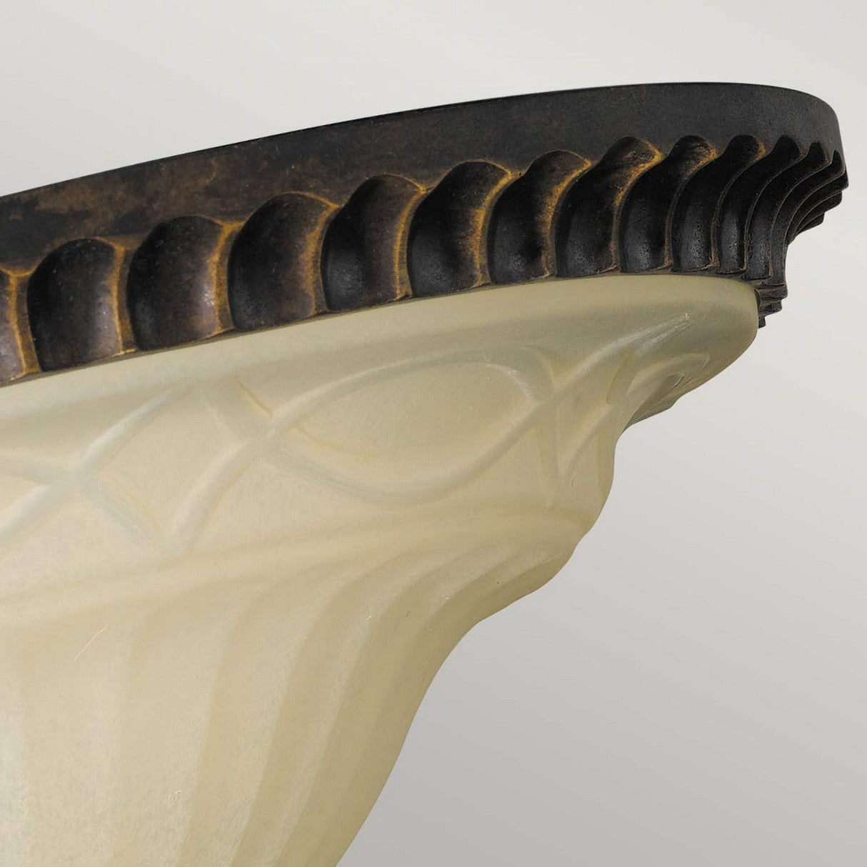 A close-up of the Drawing-1 Room 2 Light Flush in walnut highlights its Edwardian design, featuring a scalloped edge. The fixture is adorned with a bronze-colored trim and a frosted glass body with subtle patterns, set against a soft gray background.