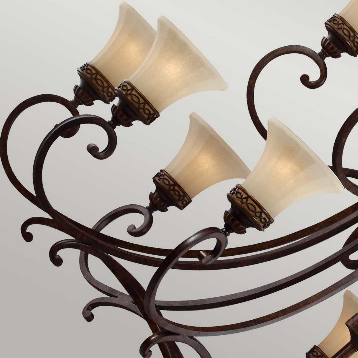 A close-up of the Drawing 18 Light Chandelier in walnut shows its Edwardian design, featuring curved bronze metalwork with six upward-facing frosted glass shades arranged in two tiers. The light fixtures are adorned with intricate metal patterns, offering a delicate blend of tradition and elegance.