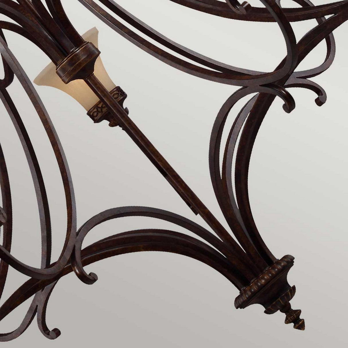 A close-up of the Drawing 18 Light Chandelier - Walnut showcases its ornate metal construction with intricate, swirling designs and small cream-colored lampshades, exuding elegance with its Edwardian design against a plain, light gray background.