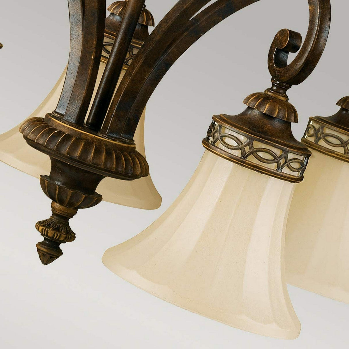 A close-up of the Drawing Room 5 Light Chandelier - Walnut reveals its ornate design with curved bronze arms and frosted glass lampshades, exuding Edwardian charm. The flared bell-shaped shades are adorned with decorative metal trim, enhancing its classic and elegant vintage appeal.