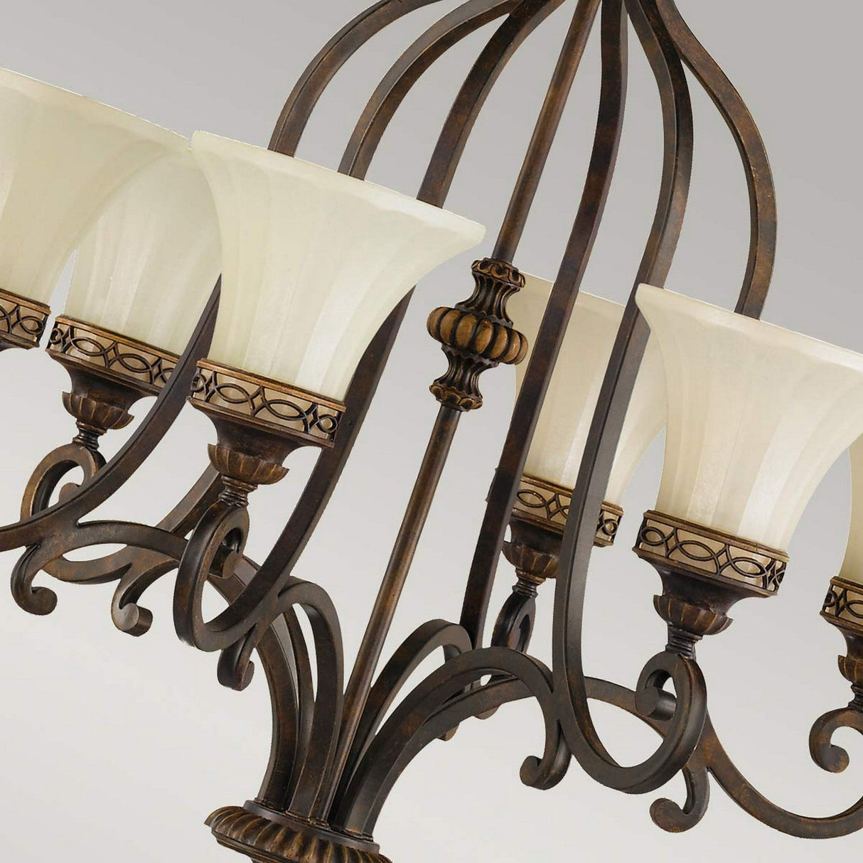 A close-up of the Drawing Room 6 Light Chandelier - Walnut, featuring an ornate Edwardian style with intricate bronze metalwork and a walnut finish. The chandelier has frosted glass lampshades that display a decorative band design, set against a soft gray background.