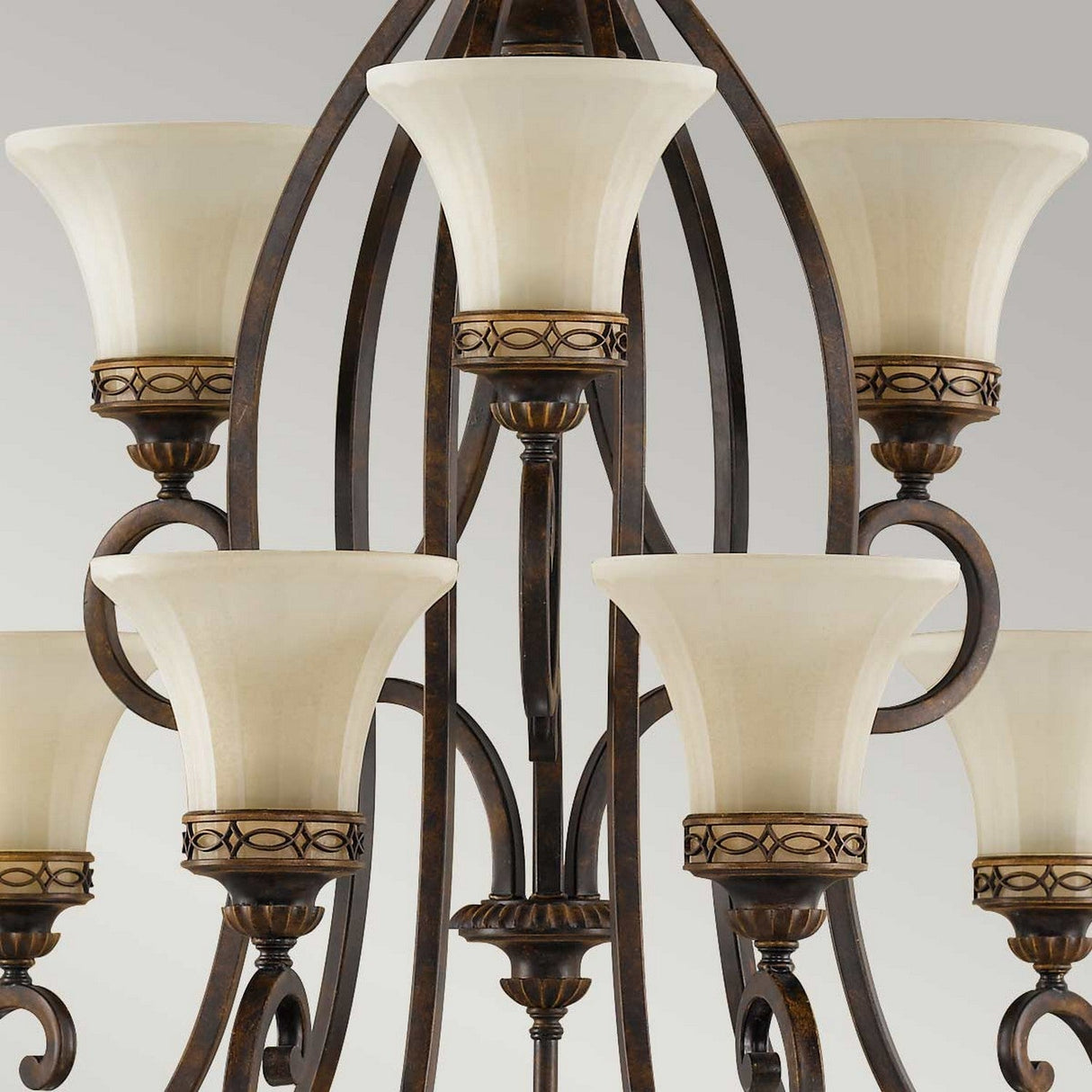 The Drawing Room 9 Light Chandelier - Walnut captures Edwardian elegance with its nine upward-facing cream-colored lampshades and decorative metal accents. Its dark, antique-finish metal frame and gracefully curved arms reflect traditional craftsmanship, beautifully set against a plain gray background.