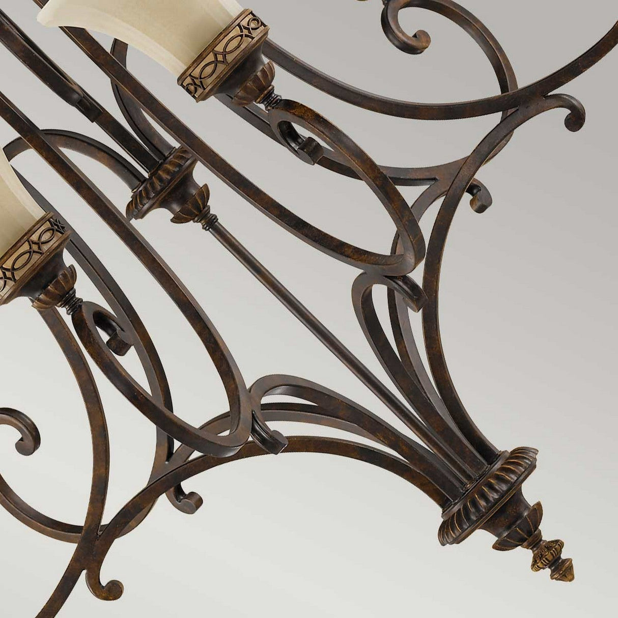 Close-up of a Drawing Room 9 Light Chandelier in a refined walnut finish, featuring ornate wrought iron scrollwork and cream-colored glass shades. The chandelier showcases traditional craftsmanship and Edwardian elegance against a neutral background.