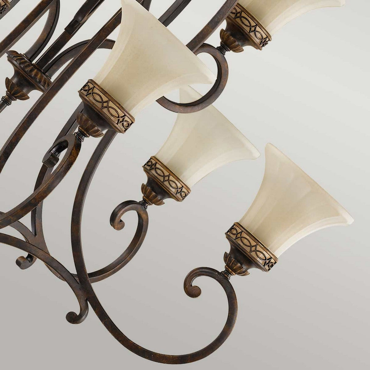 Close-up of an elegant chandelier, the Drawing Room 9 Light Chandelier - Walnut, exhibiting Edwardian elegance with its stunning bronze finish. It boasts six cream-colored, flared lampshades adorned with decorative rims. Curved metal arms radiate from the center, imparting a classic touch to this piece of traditional craftsmanship against a neutral gray background.