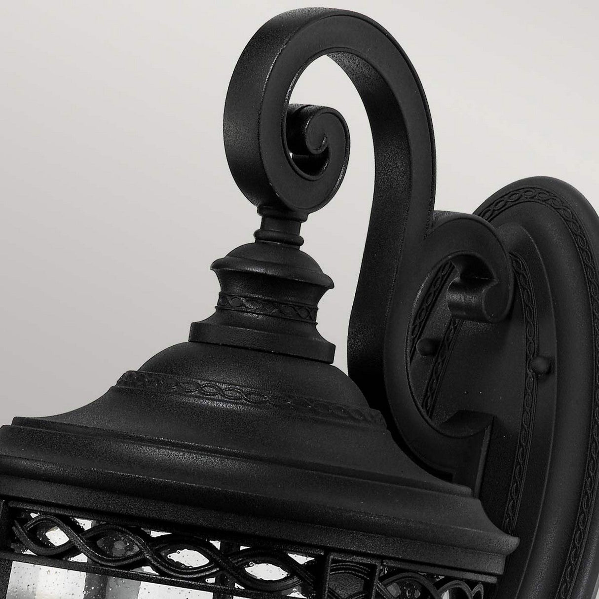 This close-up features the English Bridle 3 Light Outdoor Large Wall Lantern in black, highlighting its vintage-style design with intricate metalwork and a sleek finish. Its elegant curved arm is perfectly paired with seeded glass, all set against a light gray background.