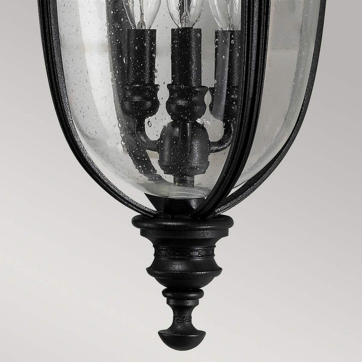 A close-up of the English Bridle 3 Light Outdoor Large Wall Lantern in a black finish, featuring a clear, seeded glass enclosure. The lantern houses three candle-style light bulbs and showcases a decorative watery texture with a classic and ornate design.