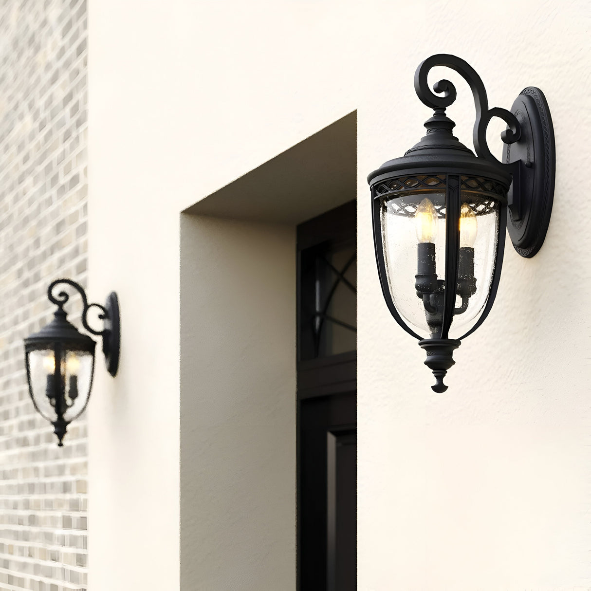 Two English Bridle 3 Light Outdoor Large Wall Lanterns in black are mounted outside on a light-colored wall near a recessed window. They are designed with clear glass panels and visible bulbs, adding an elegant and classic look to the exterior space.