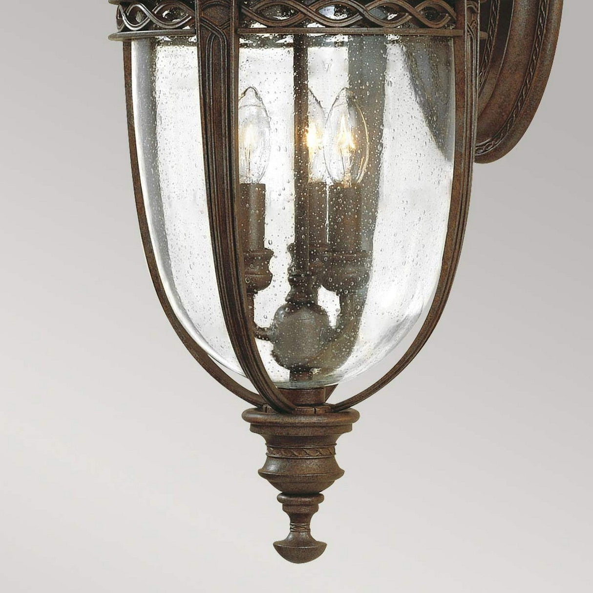 The English Bridle 3 Light Outdoor Large Wall Lantern in bronze features an antique finish, clear seeded glass panels, and accommodates three candle-shaped bulbs for a warm glow. Its intricate detailing and classic, elegant design make it ideal for enhancing your outdoor lighting ambiance.