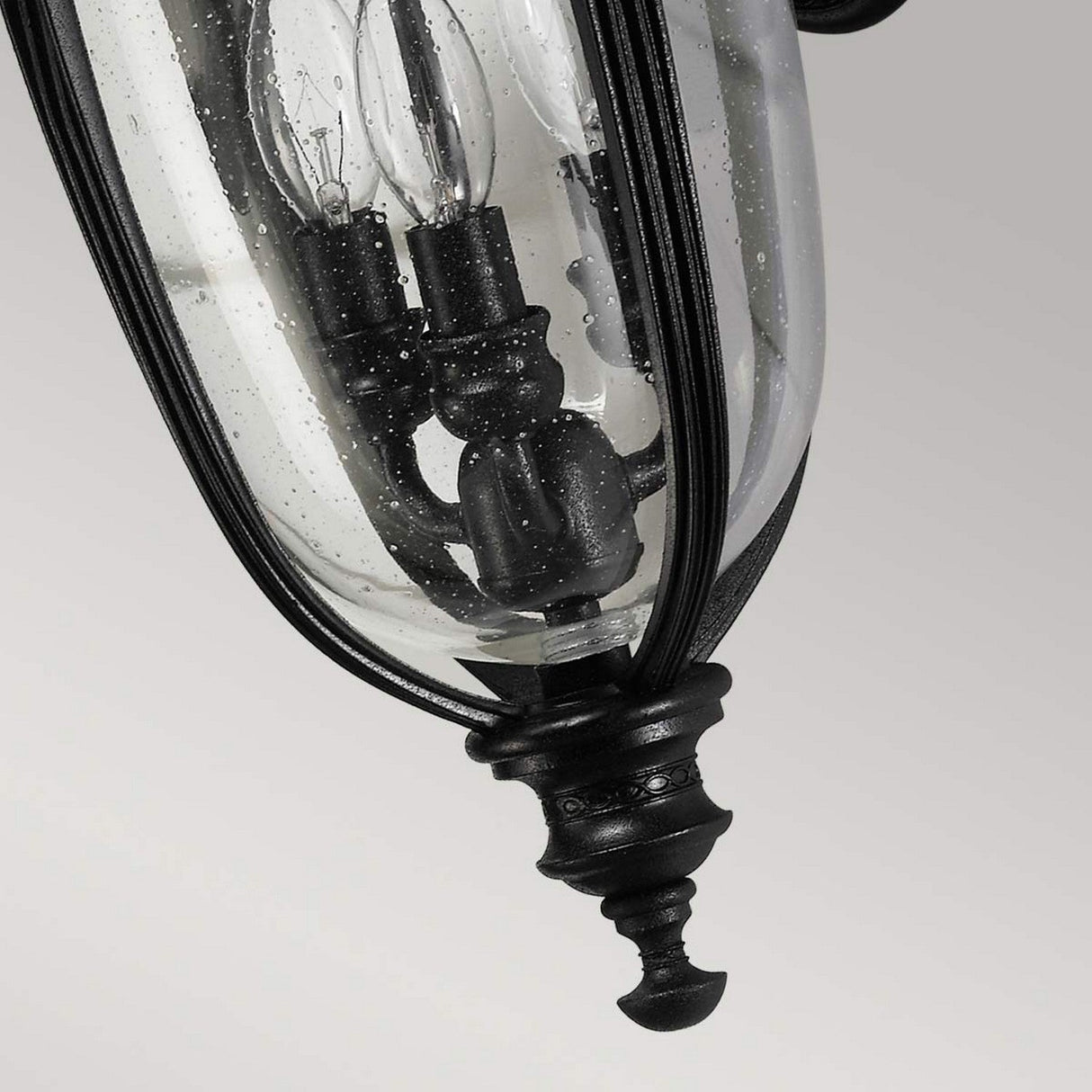 Close-up of the English Bridle 3 Light Outdoor Medium Wall Lantern in black, featuring a design with three candle-like lights inside clear seeded glass panels. The speckled glass provides texture against the plain light gray background.