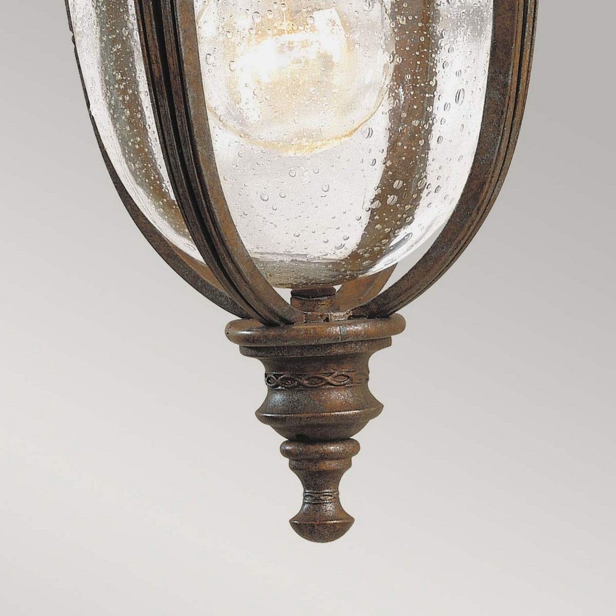 Close-up of the English Bridle 1 Light Outdoor Small Wall Lantern in a British Bronze finish, featuring a clear seeded glass shade. This intricately detailed fixture highlights the glowing bulb inside, set against a light gray background, reminiscent of a classic English Bridle Lantern.
