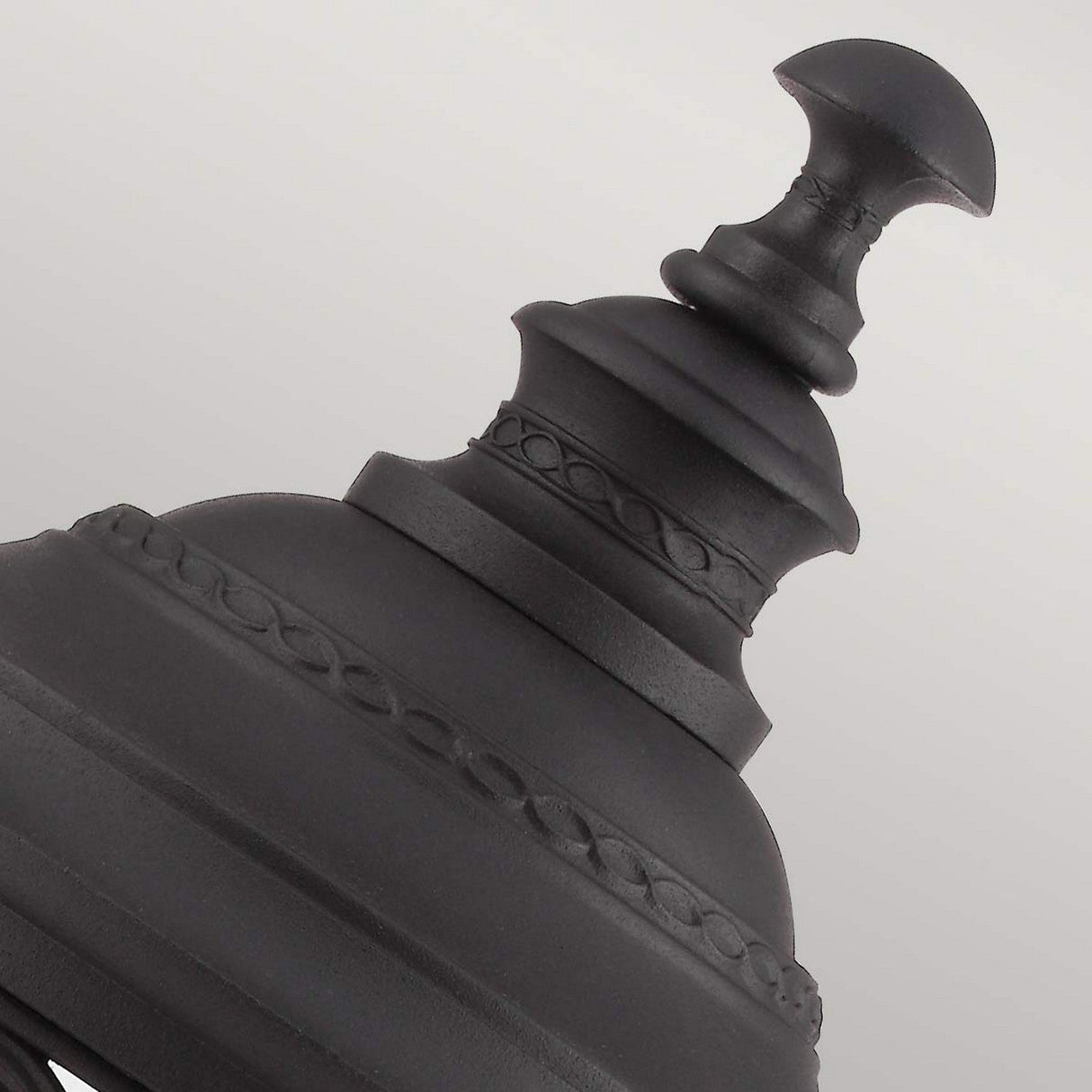Close-up of the English Bridle 3 Light Outdoor Large Pedestal in black, showcasing its intricate design with a sleek finish against a light gray background. The pedestal features a series of round, stacked segments with decorative detailing, reminiscent of elegant outdoor lighting elements.