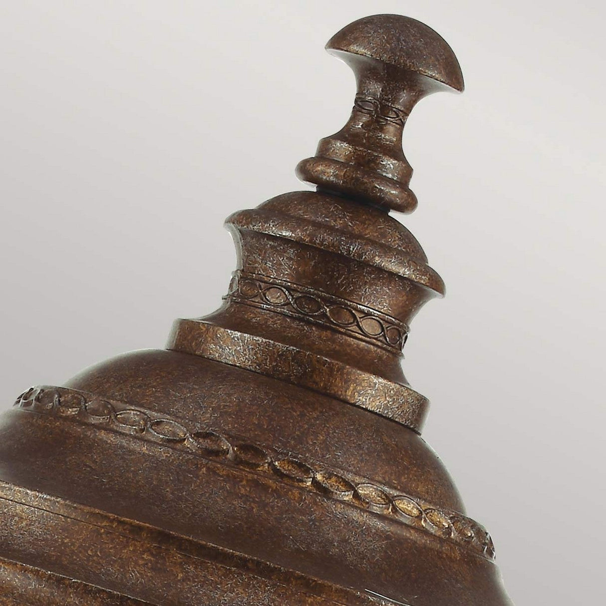 A detailed view of the English Bridle 3 Light Outdoor Large Pedestal in bronze, featuring intricate decorative bands and a smooth, rounded top set against a neutral backdrop. The aged texture enhances its vintage charm, evoking an antique outdoor pedestal light aesthetic.