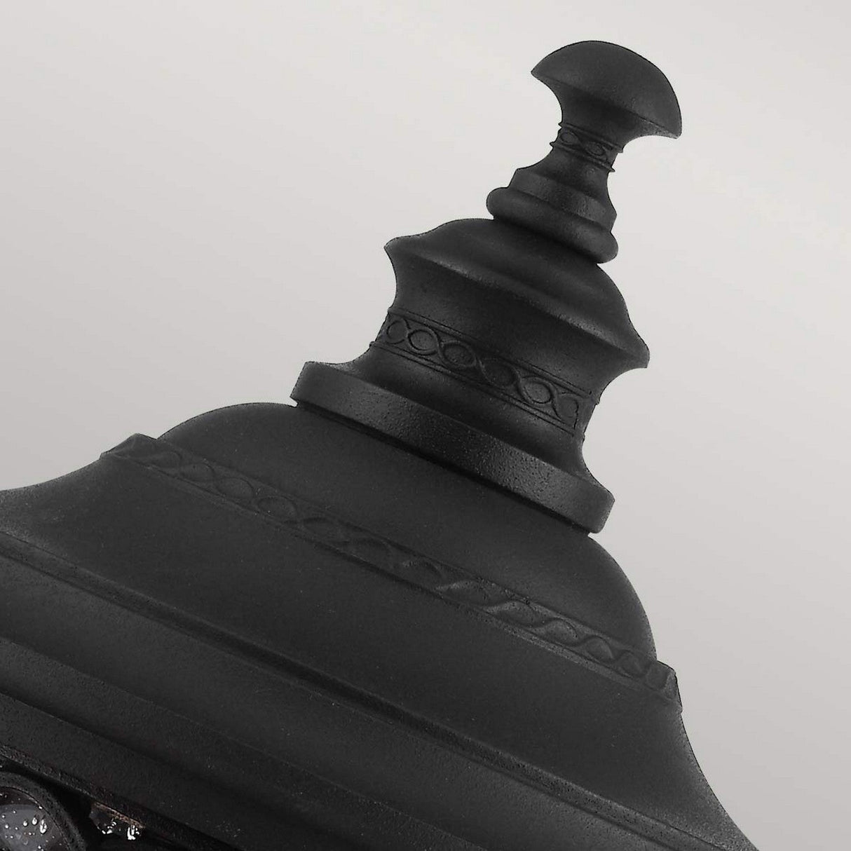Close-up of a decorative black metal finial with a sleek black finish, showcasing intricate details and a pointed top. It's set against a light gray background, reminiscent of the English Bridle 3 Light Outdoor Medium Pedestal in Black, echoing the elegance of clear seeded glass.