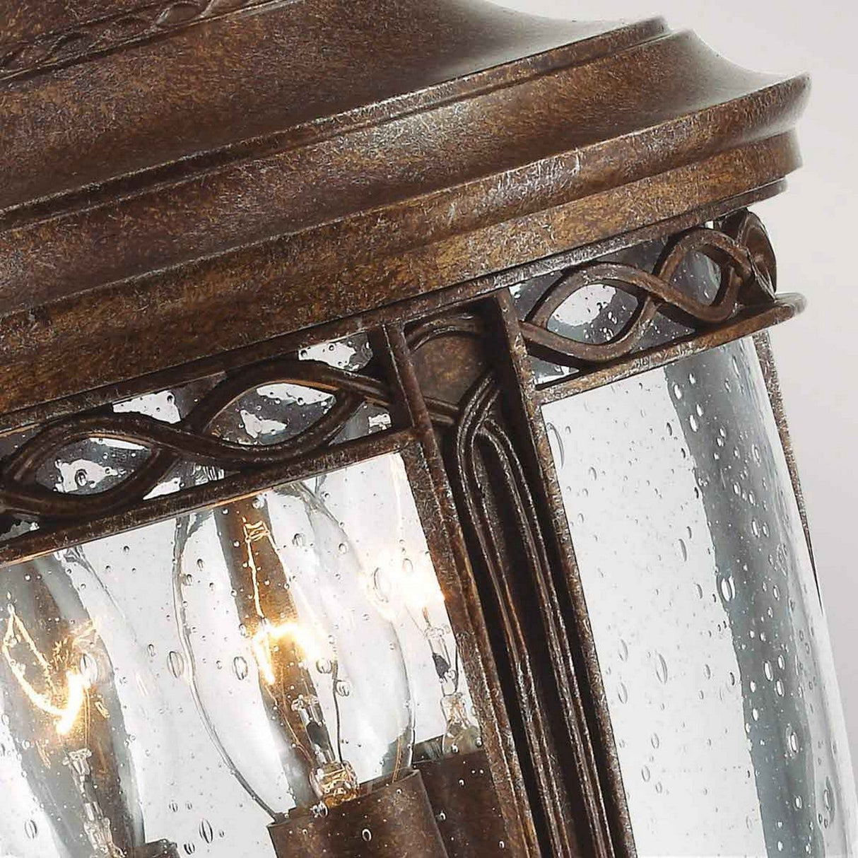 Here's a rephrased version of the sentence using the given product data:
Close-up of the English Bridle 3 Light Outdoor Medium Pedestal in Bronze, showcasing its vintage flair. The rain-speckled glass encases visible bulbs and is complemented by ornate detailing along the edges, enhancing its timeless elegance.