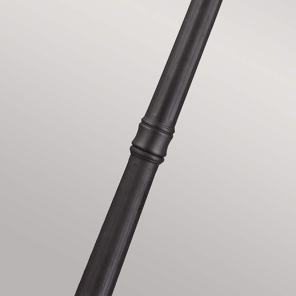 A close-up of a black metal curtain rod, featuring a textured, cylindrical design with hints of traditional elegance in the center, evokes the classic charm of an English Bridle 3 Light Large Lamp Post. The rod is set diagonally against a simple light gray background.