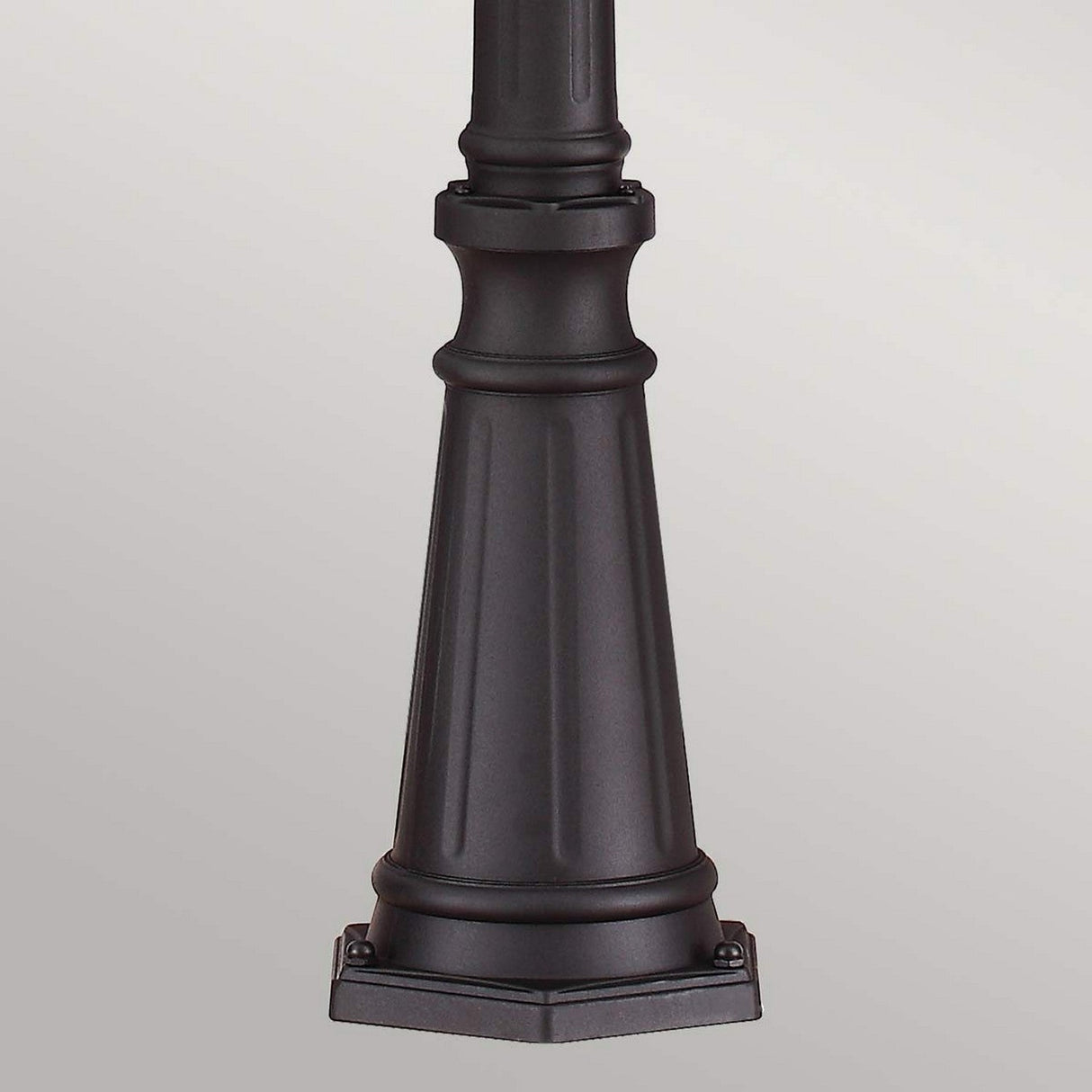 The image showcases the base of the English Bridle 3 Light Large Lamp Post in black, featuring a hexagonal shape and intricate vertical lines extending upwards. This traditional design is set against a plain gray background, epitomizing timeless outdoor lighting elegance.