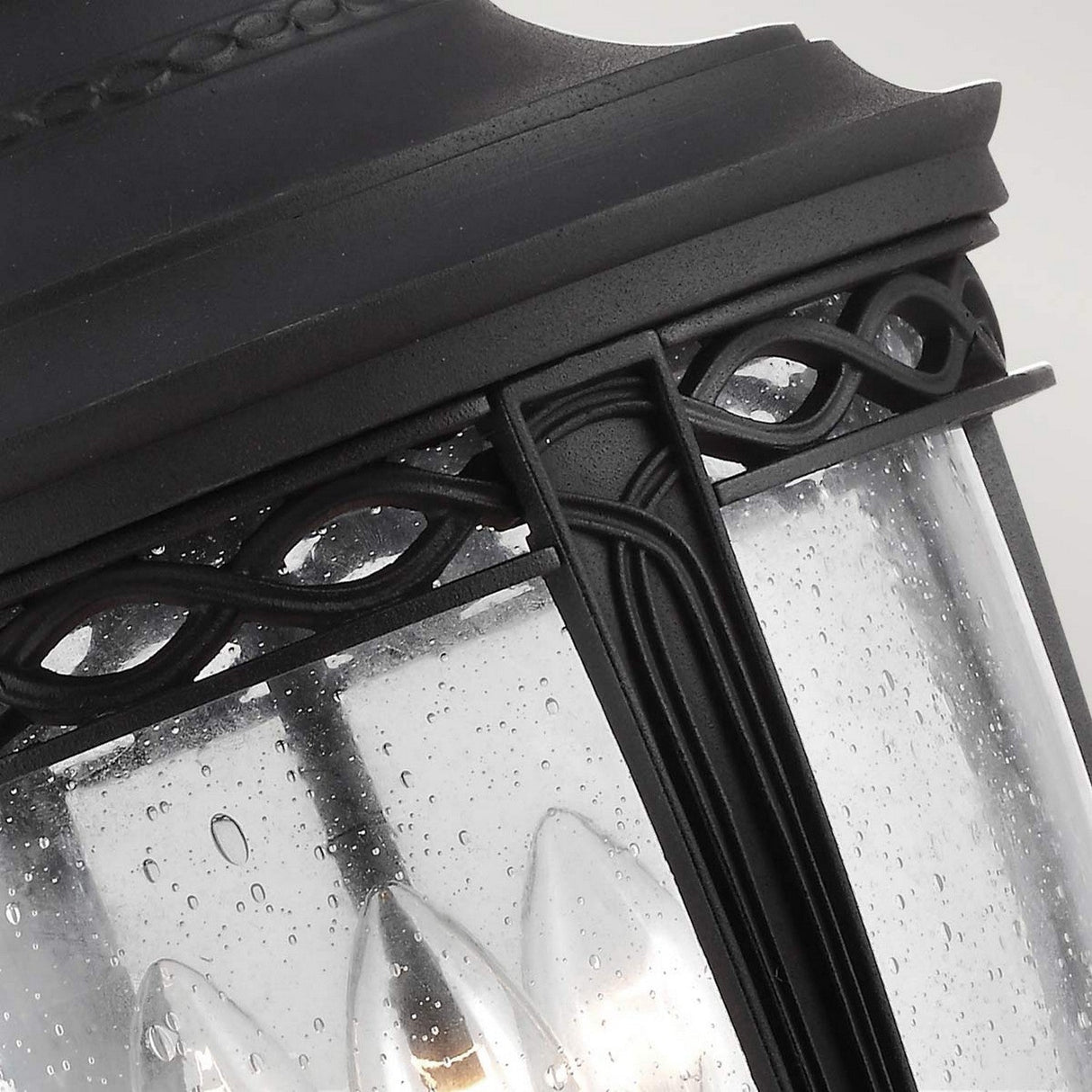 Close-up of the English Bridle 3 Light Outdoor Large Chain Lantern - Black, featuring intricate decorative detailing. The clear seeded glass panels are dotted with water droplets, evoking recent rainfall and enhancing the outdoor lighting ambiance.
