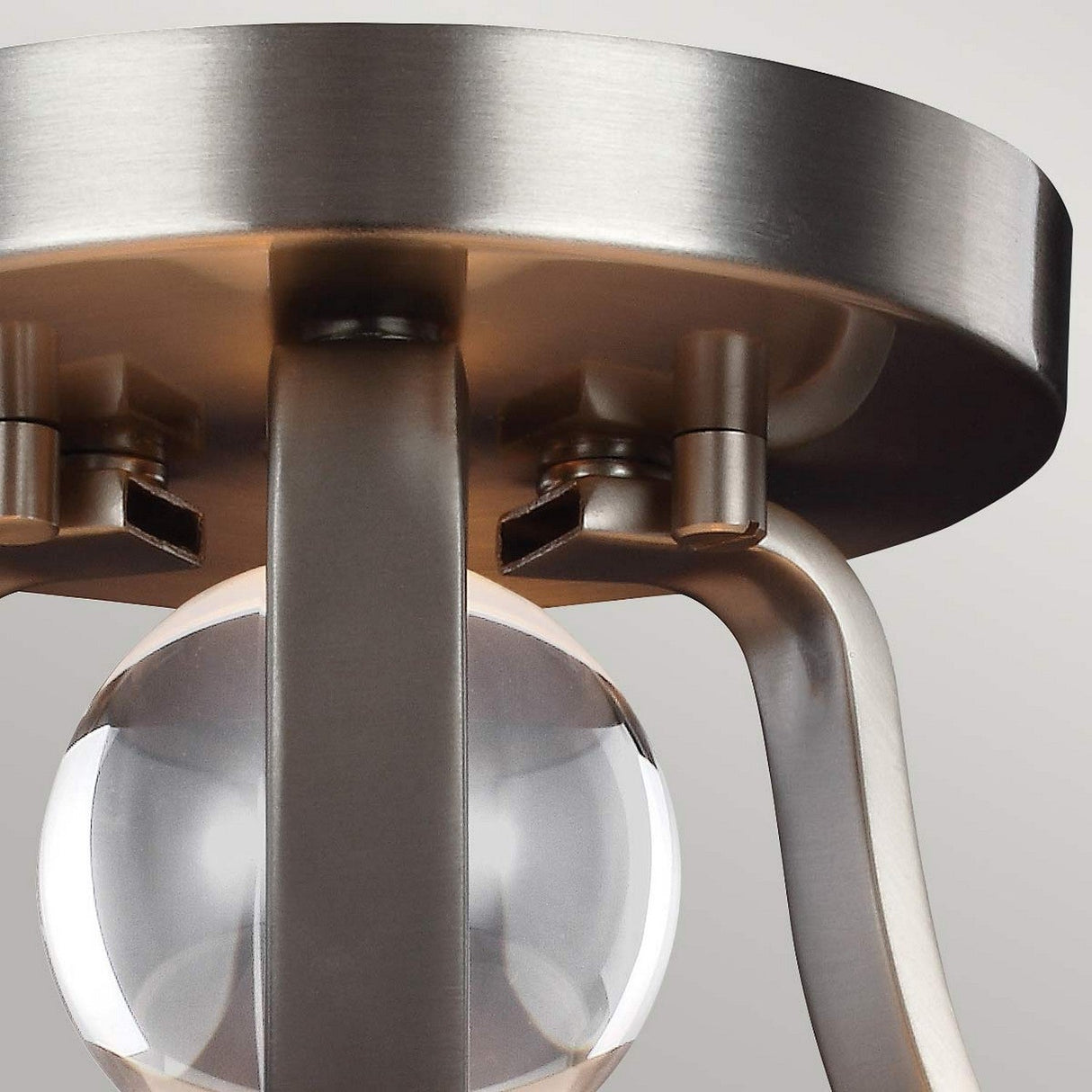 A close-up of the Evington 2 Light Semi Flush with a satin nickel finish showcases its modern design. The fixture features a circular metal base and a curved support holding a clear glass orb, beautifully distributing light against the neutral gray background.