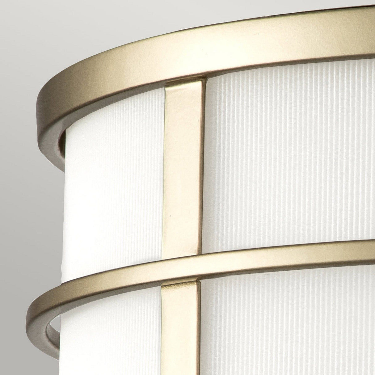 A close-up of the Fusion 3 Light Flush - Painted Natural Brass features a modern cylindrical design with ribbed glass shades and horizontal gold bands in painted natural brass framing, set against a light gray background.