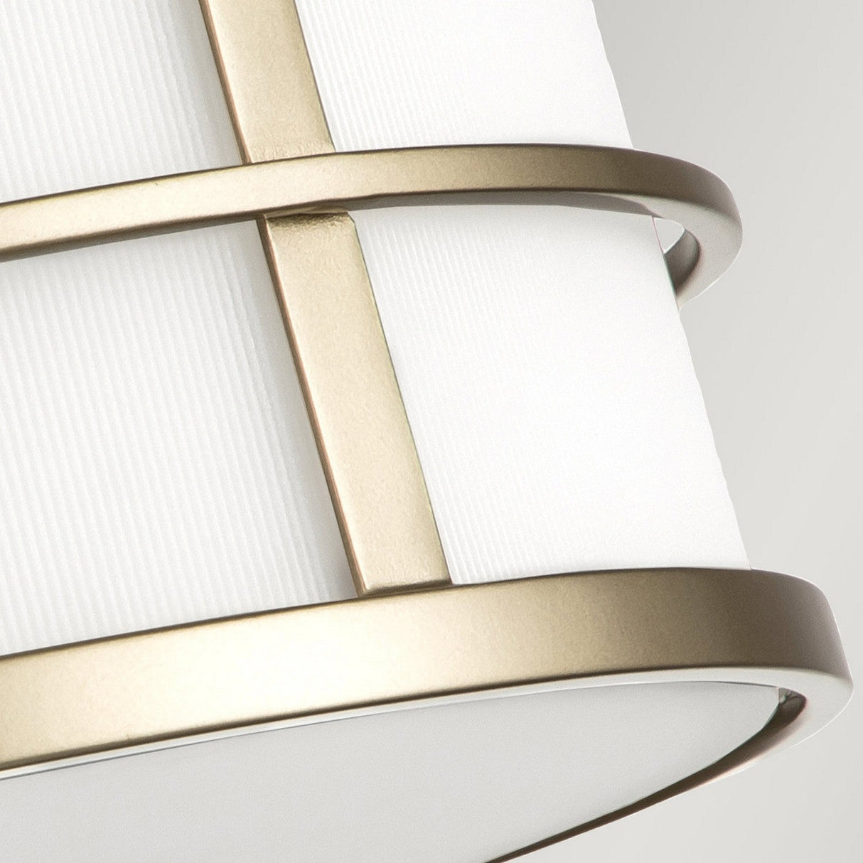 The Fusion 3 Light Flush - Painted Natural Brass features a modern cylindrical lampshade with a white fabric cover and horizontal ribbing reminiscent of ribbed glass shades. Two gold metal bands encircle the design, adding an elegant touch of painted natural brass. The lamp is set against a neutral background for a sleek appearance.