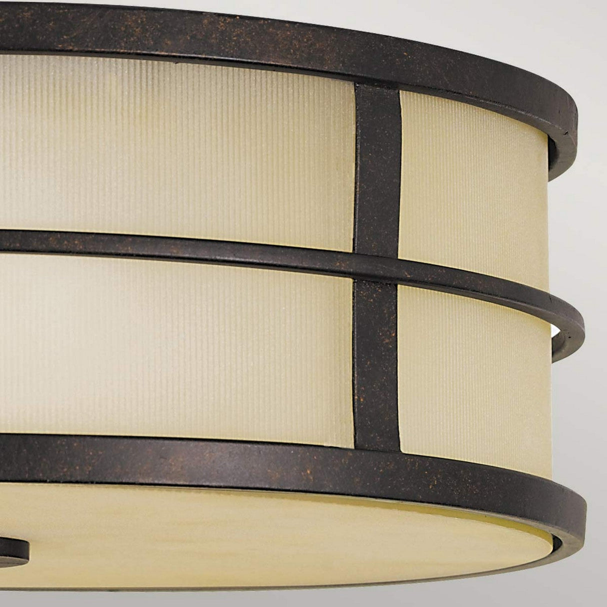 The Fusion 3 Light Flush in Grecian Bronze features a modern and minimalist design, showcasing a close-up of its round ceiling light fixture with a ribbed, cream-colored surface and Grecian Bronze metal bands, beautifully enhancing the ambient atmosphere with its soft glow.