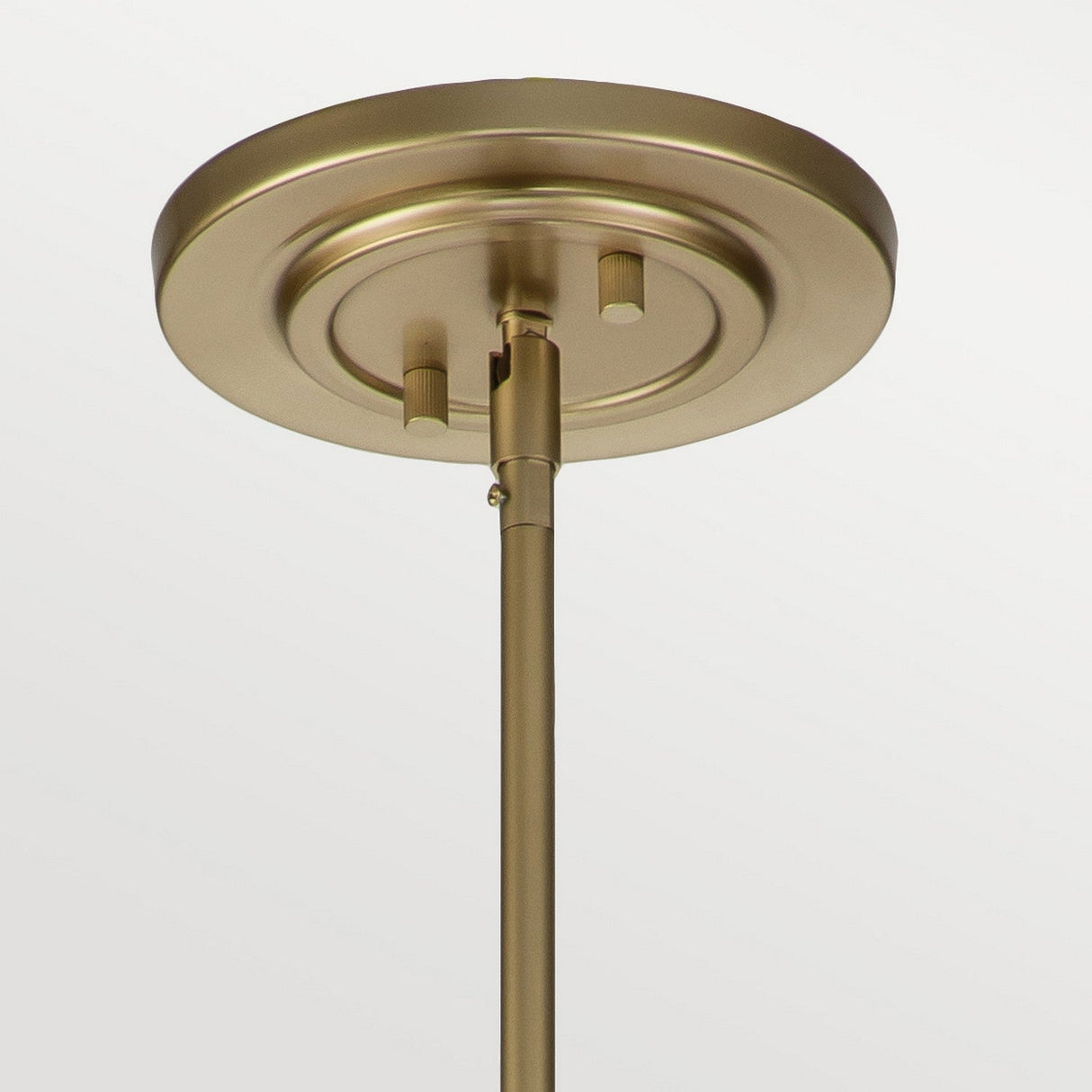 Close-up of the Fusion 3 Light Large Chandelier in Painted Natural Brass, showcasing a circular ceiling fixture base with a rod extending downward. Its sleek, modern design contrasts beautifully against the neutral background, enhanced by amber ribbed glass accents.
