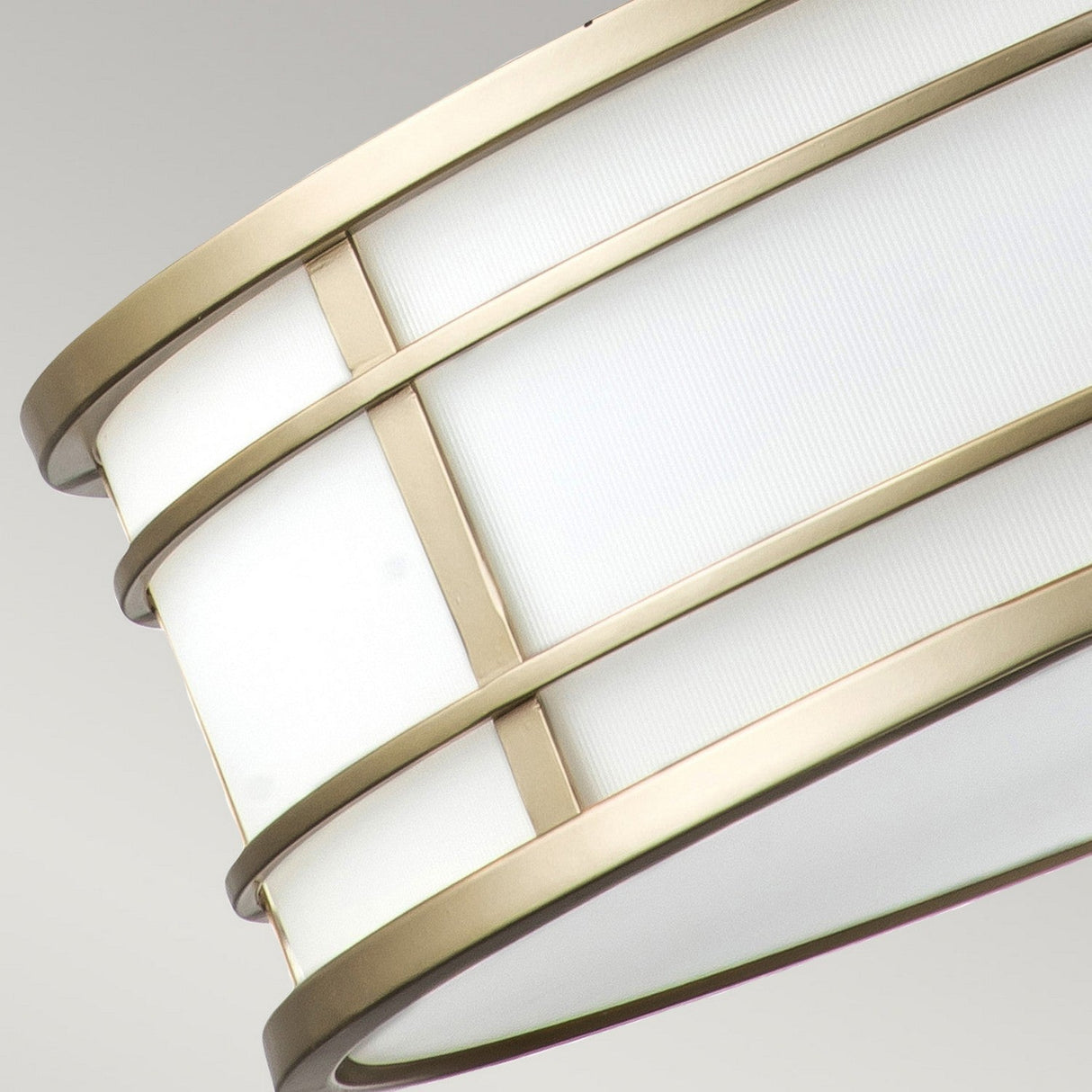 A detailed view of the Fusion 3 Light Large Chandelier in painted natural brass showcases its sleek cylindrical design, with natural brass bands. Its white translucent surface gently diffuses light against a neutral backdrop, offering an elegant contrast.
