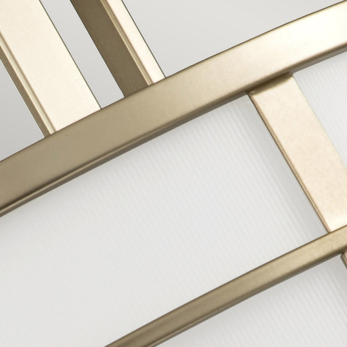 Close-up of the Fusion 3 Light Semi Flush in Painted Natural Brass featuring an abstract geometric design with intersecting metallic gold bars over a textured white background. The composition emphasizes symmetry, contrast, and shiny metallic textures, enhanced by a natural brass finish that adds elegance.