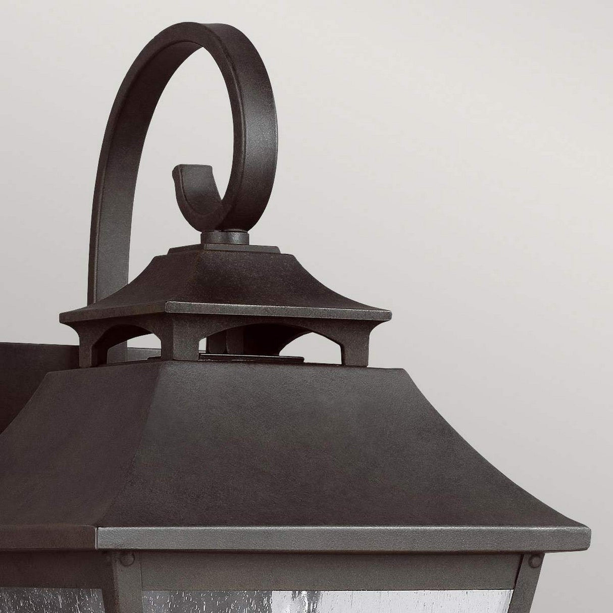 Close-up of the Galena 1 Light Outdoor Medium Wall Lantern in Sable, showcasing its decorative black metal frame and curved top bracket. This lantern features a rectangular design with seeded glass panels, set against a plain light gray background, ensuring excellent weather resistance thanks to its IP44 rating.
