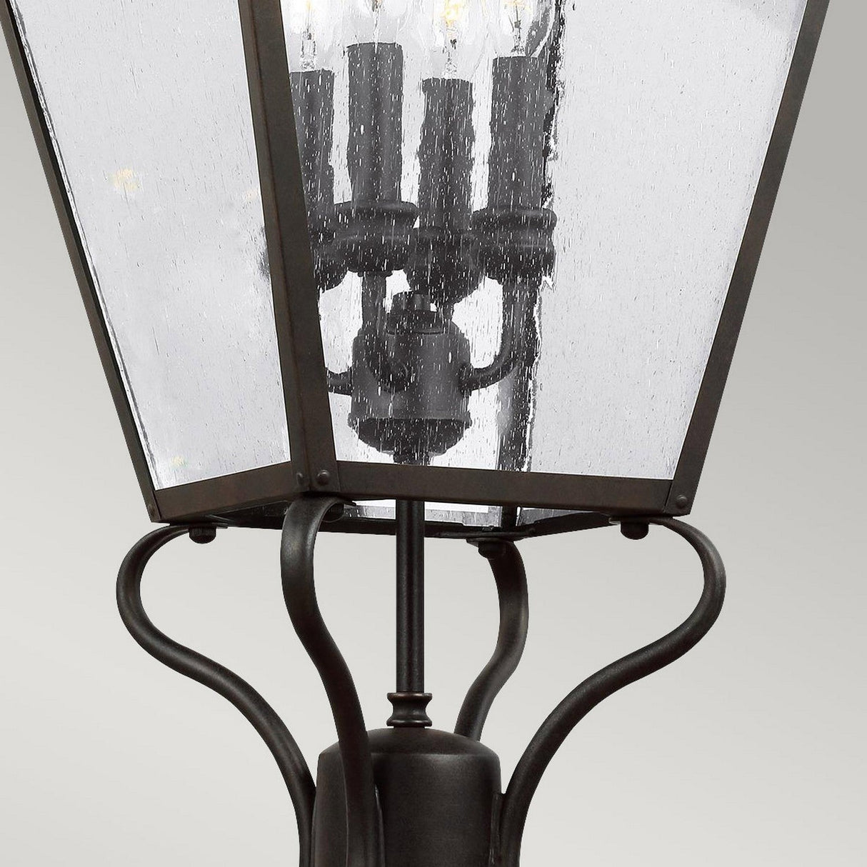 Close-up of a Galena 4 Light Lamp Post - Grey, showcasing its vintage design. This grey outdoor lantern features four candle-shaped light fixtures visible through seeded glass panes and is mounted on a metal post adorned with elegant curved details.